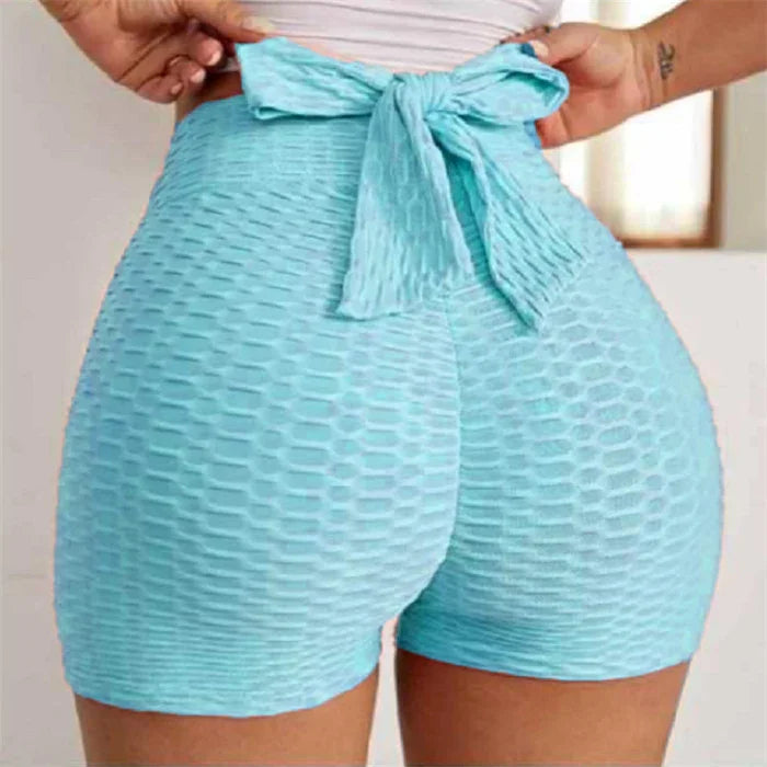 Light blue textured high waisted shorts with bow tie detail on a woman indoors