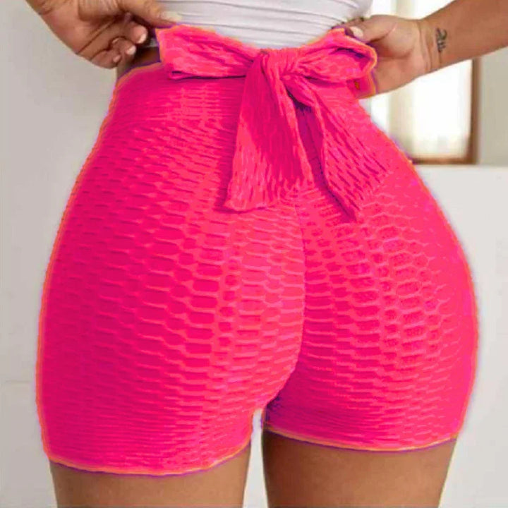 High-waisted textured neon pink shorts with bow tie, close-up indoors