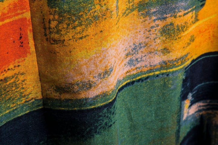Close-up of textured fabric with abstract brushstroke patterns in orange, yellow, green, and black