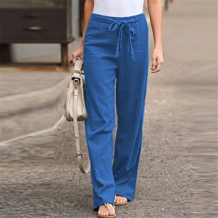 Woman wearing blue drawstring linen pants with beige handbag and sandals walking outdoors