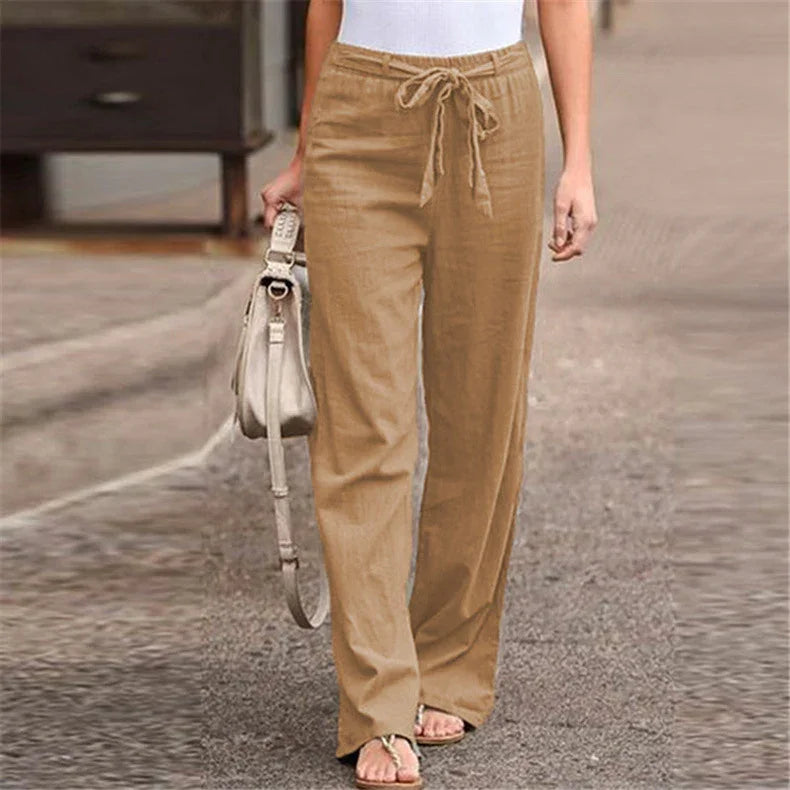 woman wearing tan drawstring linen pants with white top and beige handbag walking on street