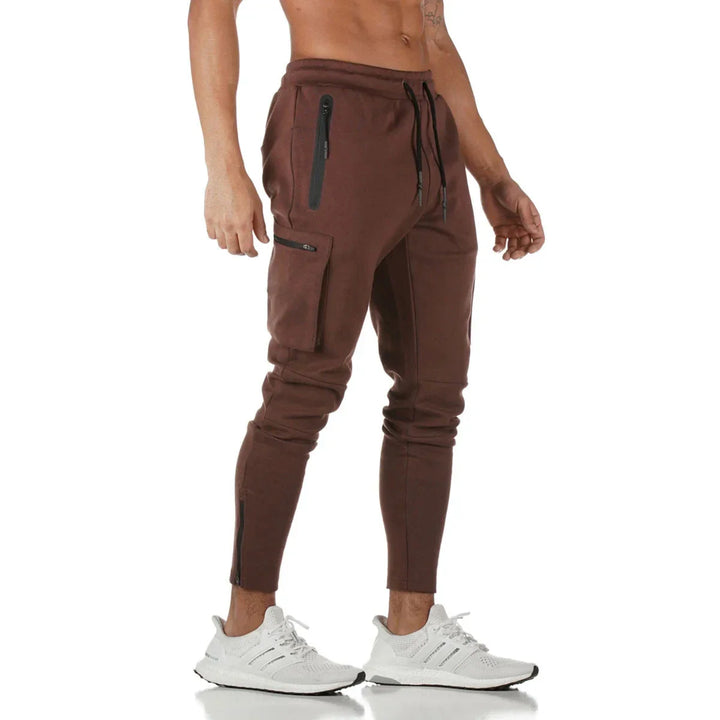 Man wearing brown slim-fit jogger pants with zippered pockets and white athletic sneakers
