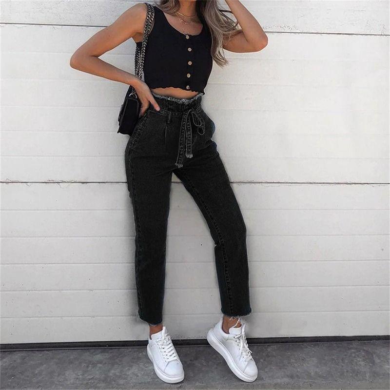 Woman wearing high-waisted black jeans with belt, black buttoned crop top, white sneakers, and black shoulder bag