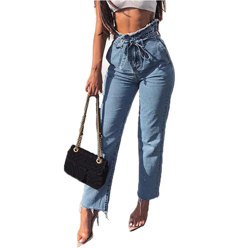 woman wearing high-waisted paperbag jeans with a bow belt, holding black handbag, and transparent heels