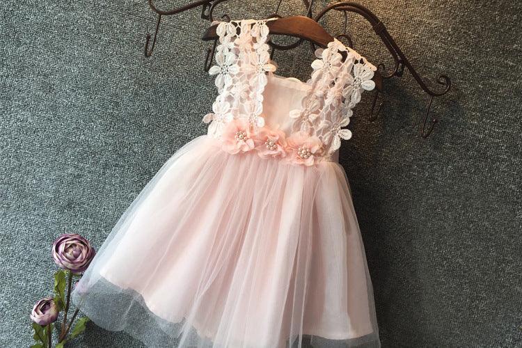 Pink toddler dress with floral lace straps, tulle skirt, and flower embellishments hanging on a decorative metal hanger