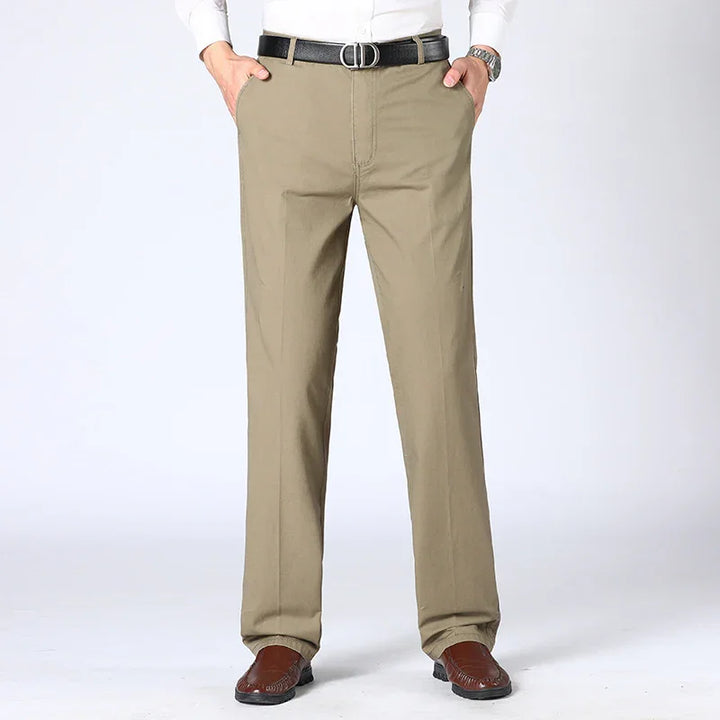 Men's beige casual pants paired with brown shoes and black belt, front view on plain background