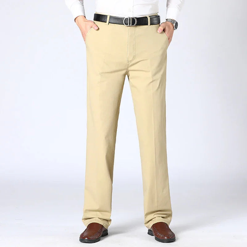 Man wearing beige casual trousers with black belt and brown shoes on white background