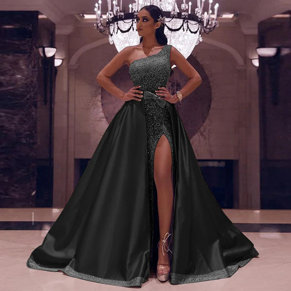 Elegant woman in black one-shoulder evening gown with thigh-high slit posing in grand hall