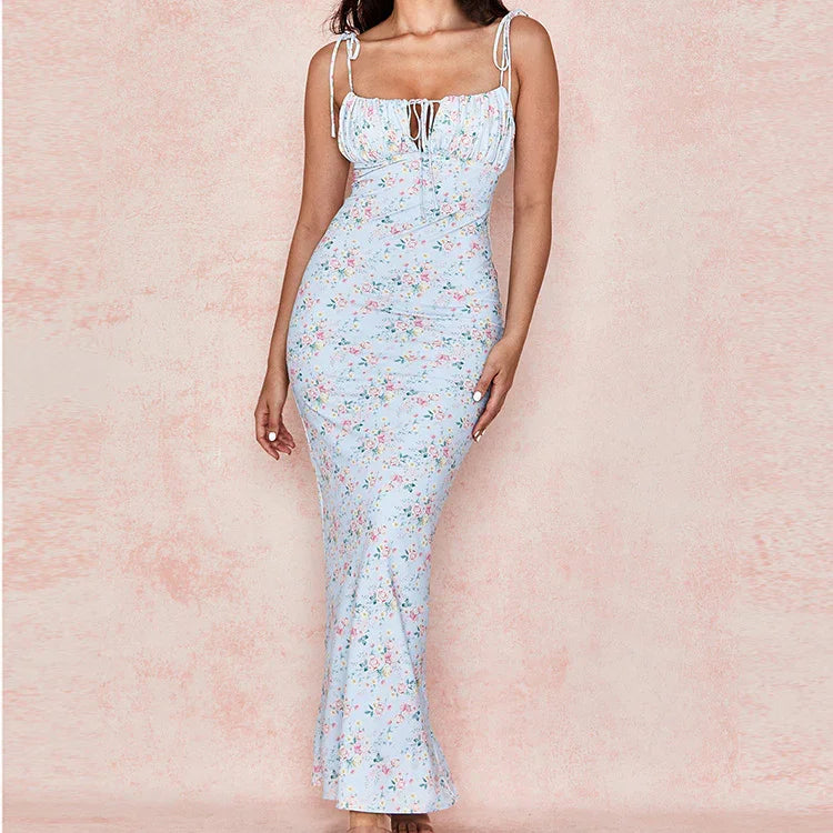 Woman wearing a light blue floral maxi dress with tie straps and ruched bust against a soft pink background