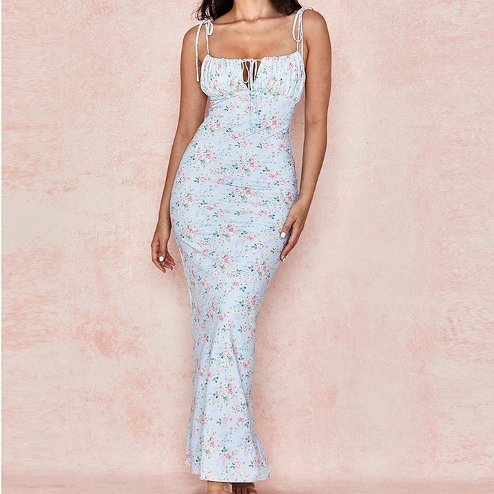 Woman wearing a light blue floral maxi dress with tie straps and ruched bust against a soft pink background