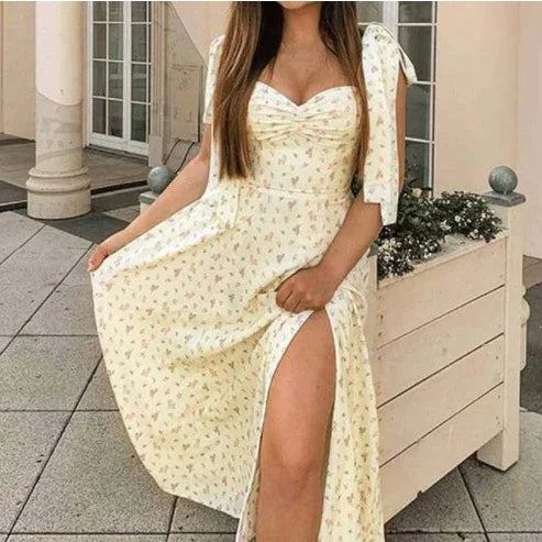 Woman wearing a light yellow floral dress with side slit and tie shoulder straps standing outdoors