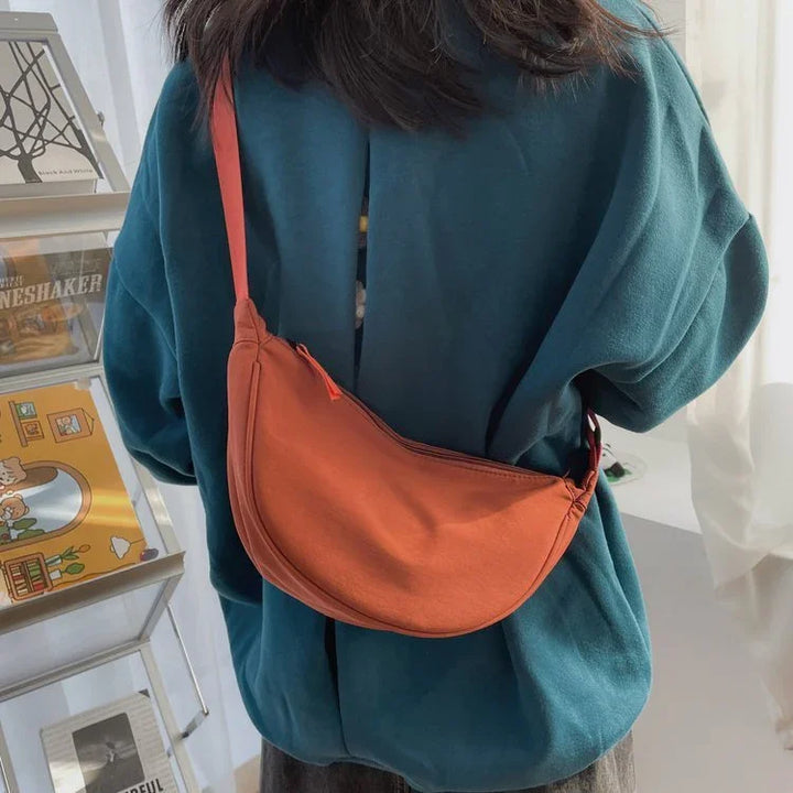 Person wearing teal sweater carrying orange crescent-shaped shoulder bag indoors