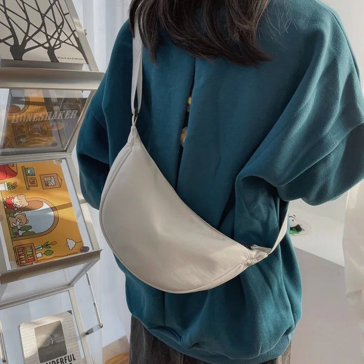 Minimalist cream crescent shoulder bag worn on back with casual teal sweatshirt indoors