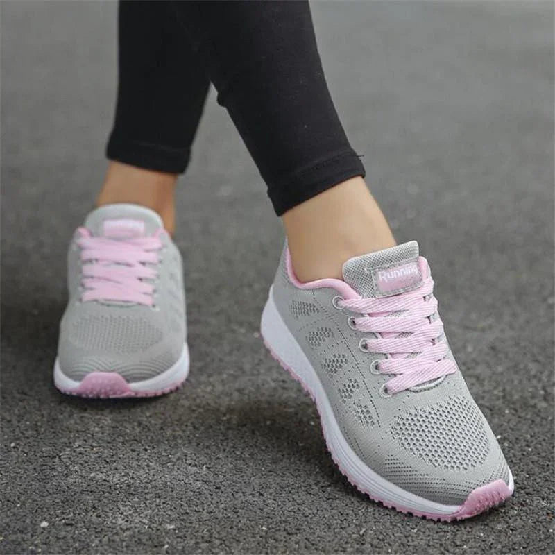 Close-up of gray and pink running shoes with pink laces worn with black leggings on asphalt