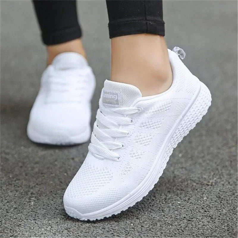 Close-up of white breathable knit sneakers worn with black leggings on asphalt surface