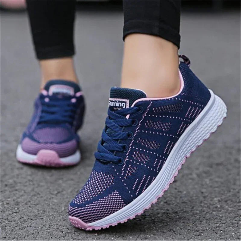 Close-up of navy and pink running shoes with white soles worn by person on asphalt