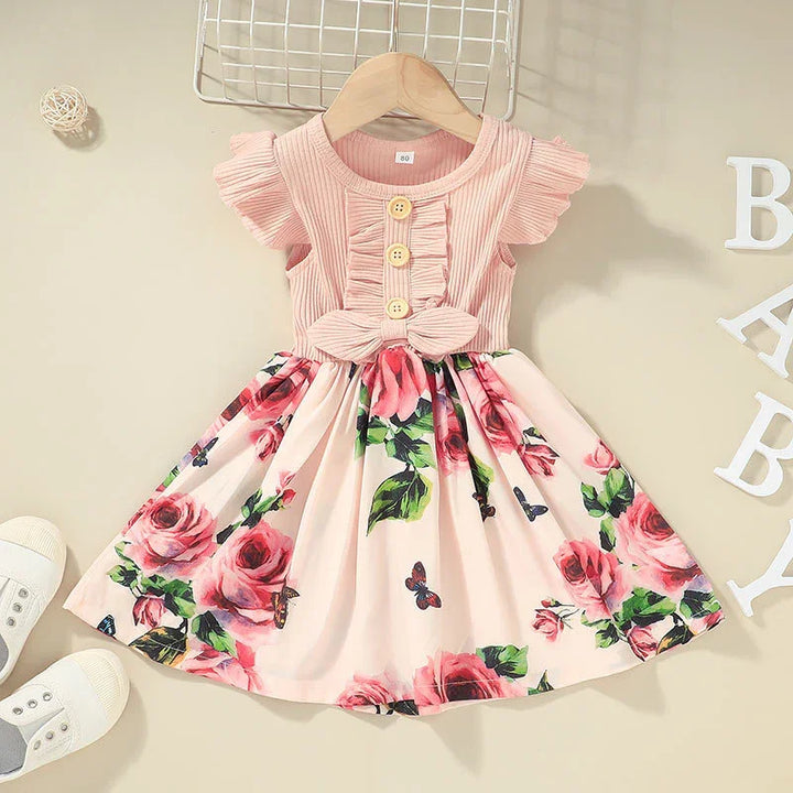 Pink baby girl dress with ribbed bodice, wooden buttons, bow detail, and floral skirt on hanger
