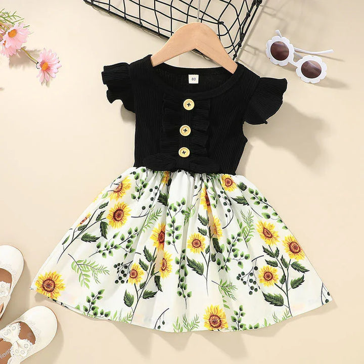 Toddler dress with black ruffle top and sunflower print skirt on hanger, white shoes and sunglasses