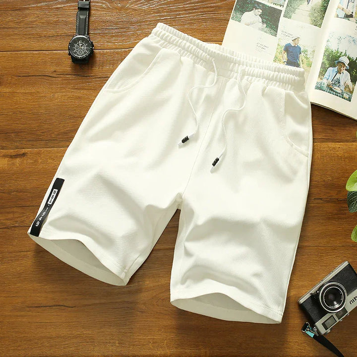White casual shorts with drawstring and side pocket on wooden surface, wristwatch and camera nearby