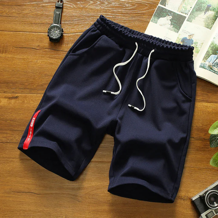 Navy blue men's casual shorts with white drawstrings and red side tag on wooden surface