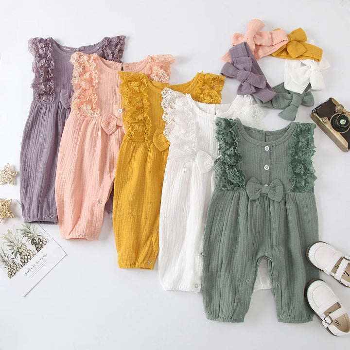 Five pastel-colored baby rompers with lace ruffles and matching bow headbands, vintage camera and white baby shoes