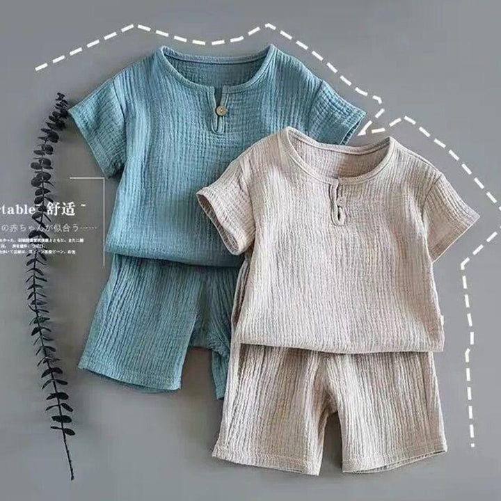 Two soft textured short sleeve toddler outfits with shorts, one blue and one beige, on gray background