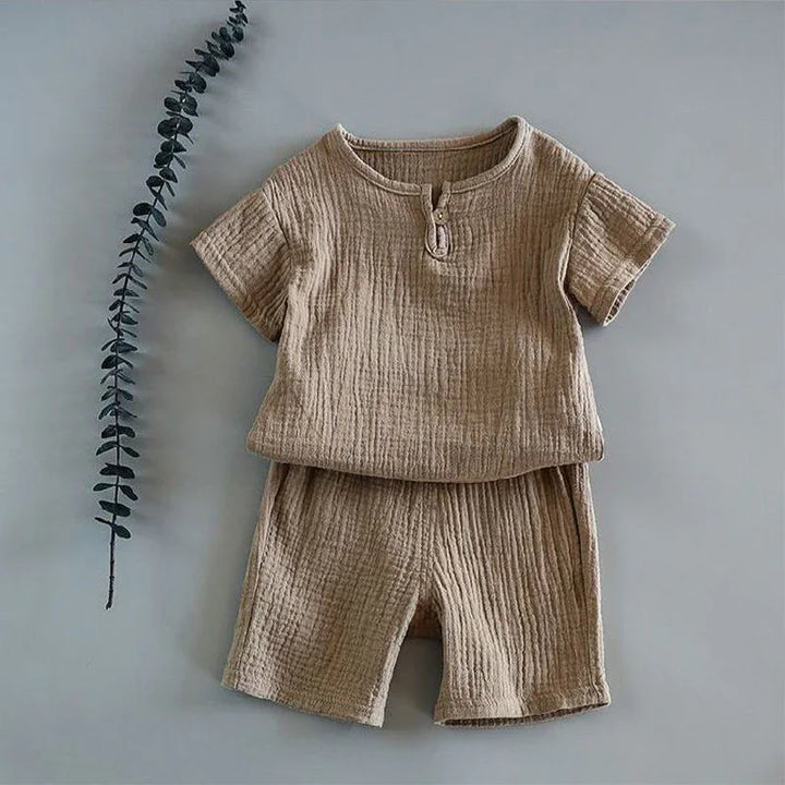 Beige textured cotton baby outfit with short sleeves and shorts on gray background with eucalyptus branch