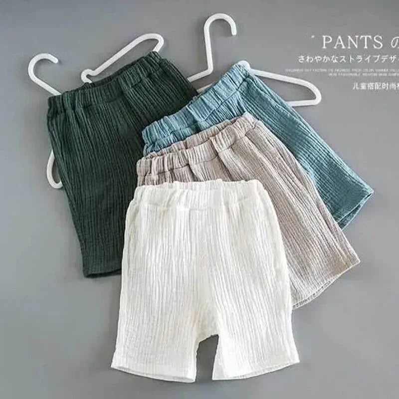 Four pairs of soft, ribbed fabric baby shorts in white, beige, blue, and dark green on white hangers