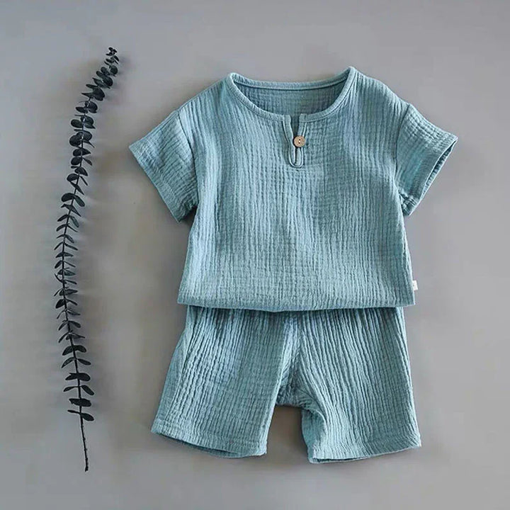 Light blue short-sleeve toddler outfit with button detail and matching shorts on grey background