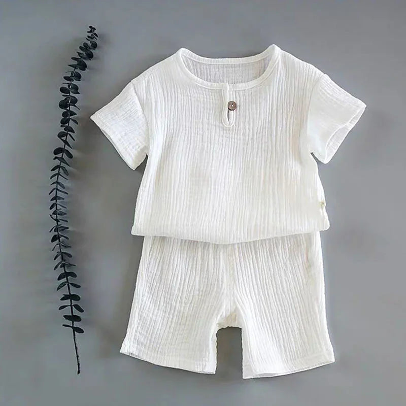 White textured short-sleeve baby outfit with button detail on gray background and decorative twig