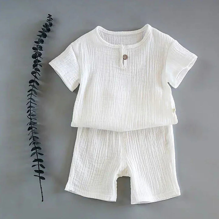 White textured short-sleeve baby outfit with button detail on gray background and decorative twig