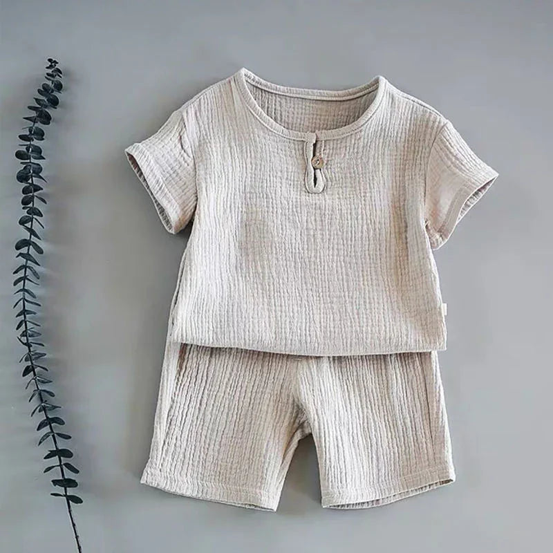 Beige textured short sleeve top and shorts set for toddlers on gray background with eucalyptus branch