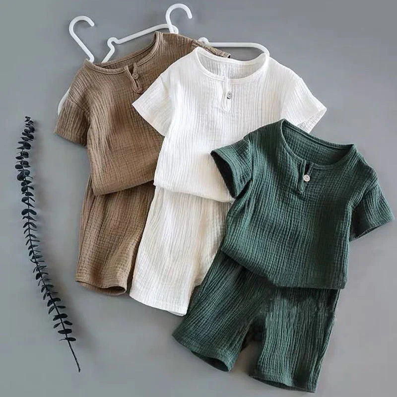 Three sets of ribbed cotton toddler summer outfits in brown, white, and green with short sleeves and buttons on gray background