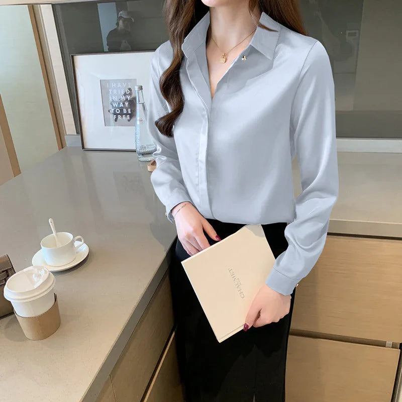 Woman wearing light blue collared shirt and black skirt holding a beige notebook in modern office kitchen