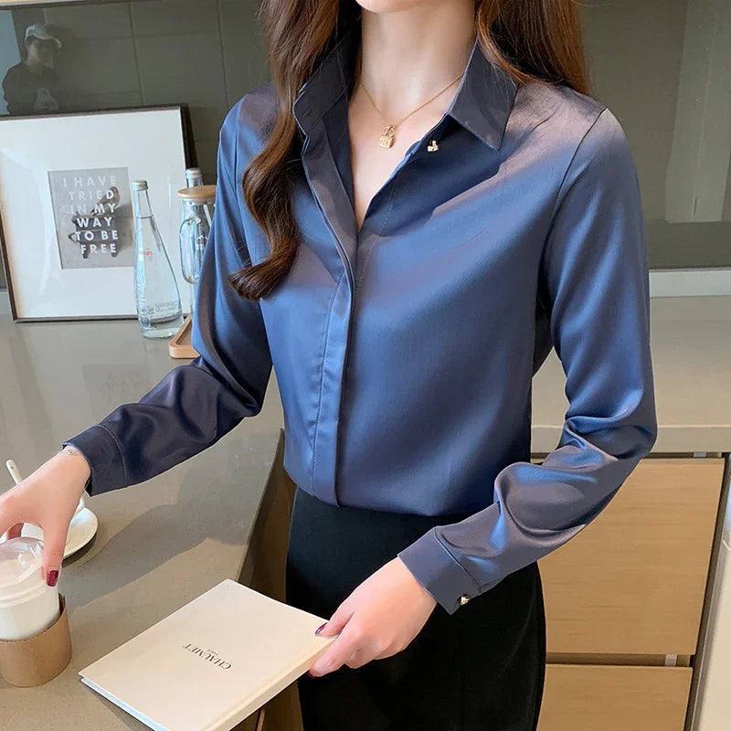 Woman wearing blue satin blouse and black skirt holding a book and disposable cup in modern kitchen