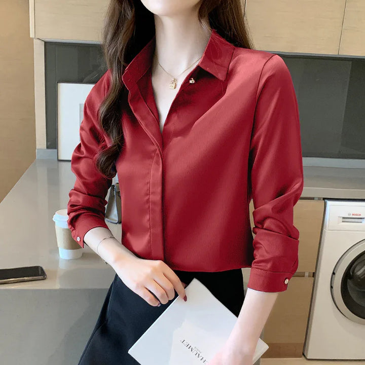 Woman wearing a red satin blouse and black skirt holding a white folder in a modern kitchen