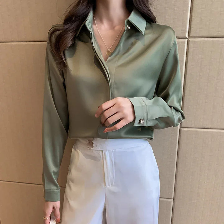 Woman wearing a sage green satin blouse with pearl button details and white high-waisted pants