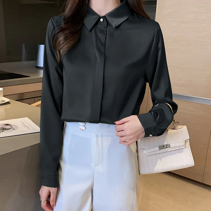 Woman wearing black satin blouse tucked into high-waisted white pants holding beige handbag