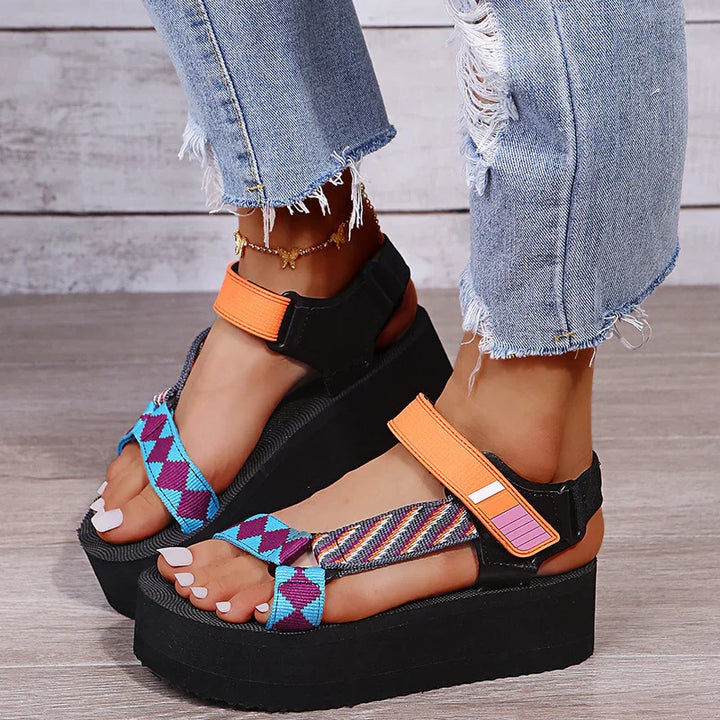 Wedge platform sandals with colorful patterned straps and orange accents worn with distressed denim jeans