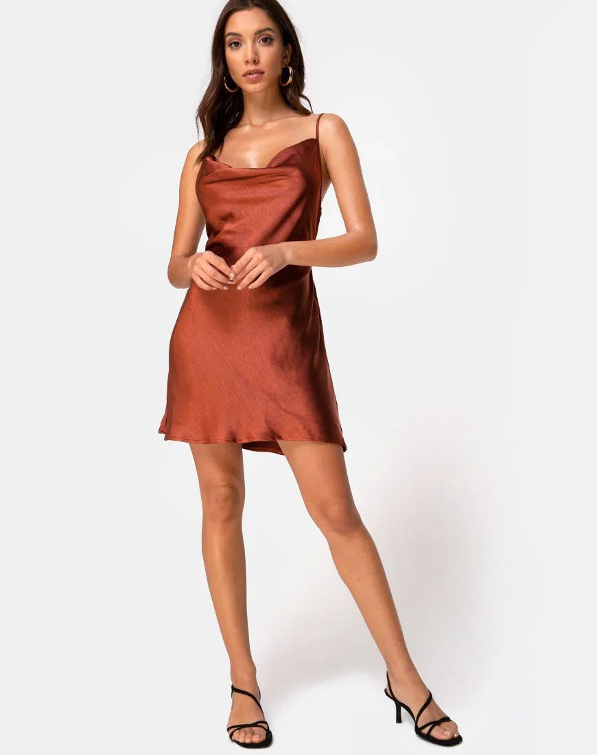 Woman wearing rust-colored satin slip dress with thin straps and black heeled sandals against white background