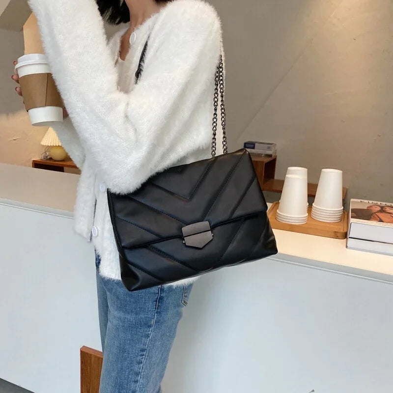 Woman wearing white fuzzy sweater and blue jeans holding coffee cup with black leather quilted chain shoulder bag