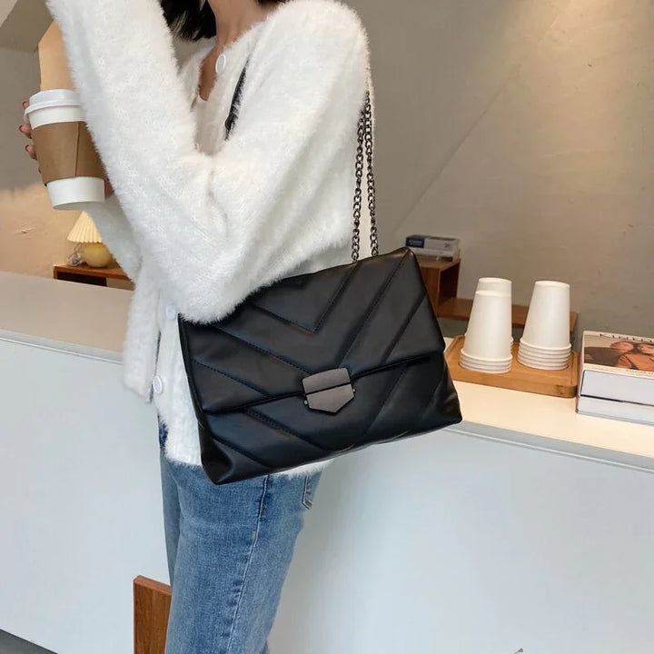 Woman wearing white fuzzy sweater and blue jeans holding coffee cup with black leather quilted chain shoulder bag