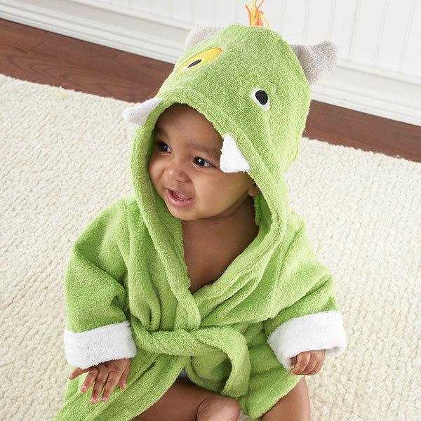 Smiling baby wearing green dinosaur hooded bathrobe sitting on cream carpet