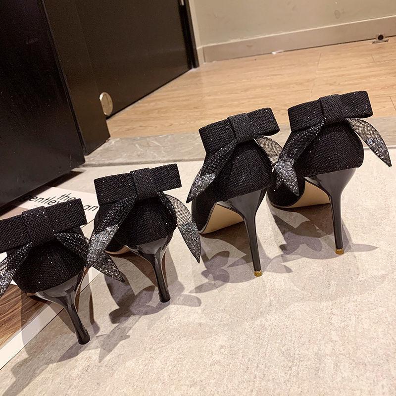 Pair of black high heel shoes with glittery bows on back, standing on floor near door