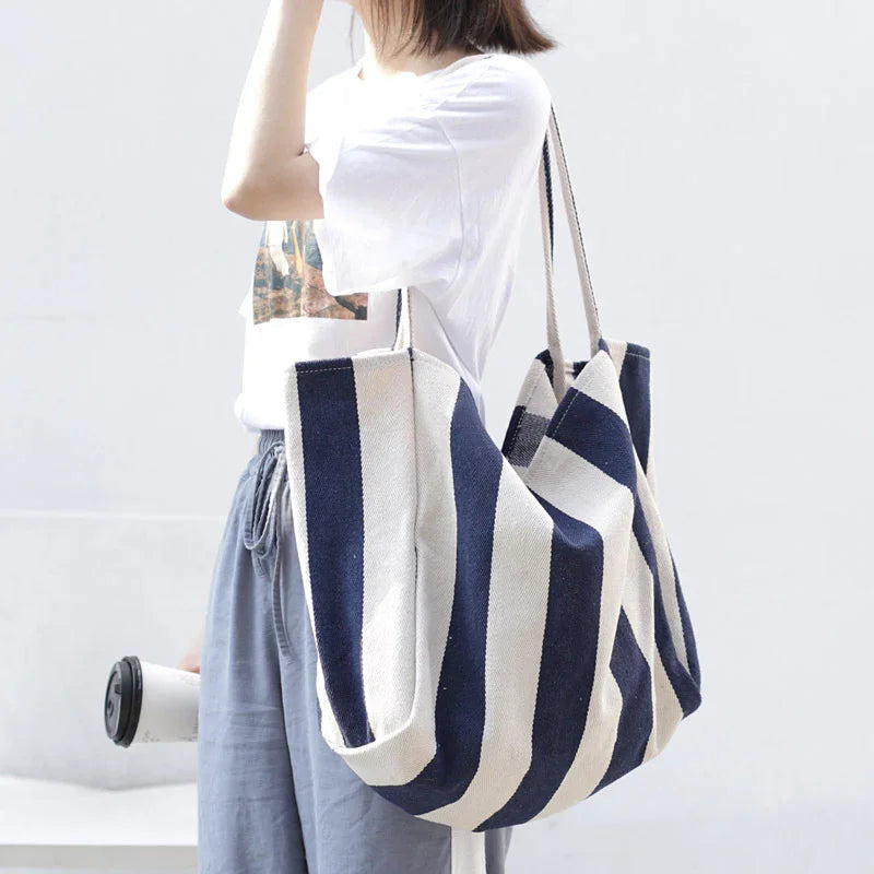 Woman in casual outfit holding a large navy and white striped tote bag and a coffee cup