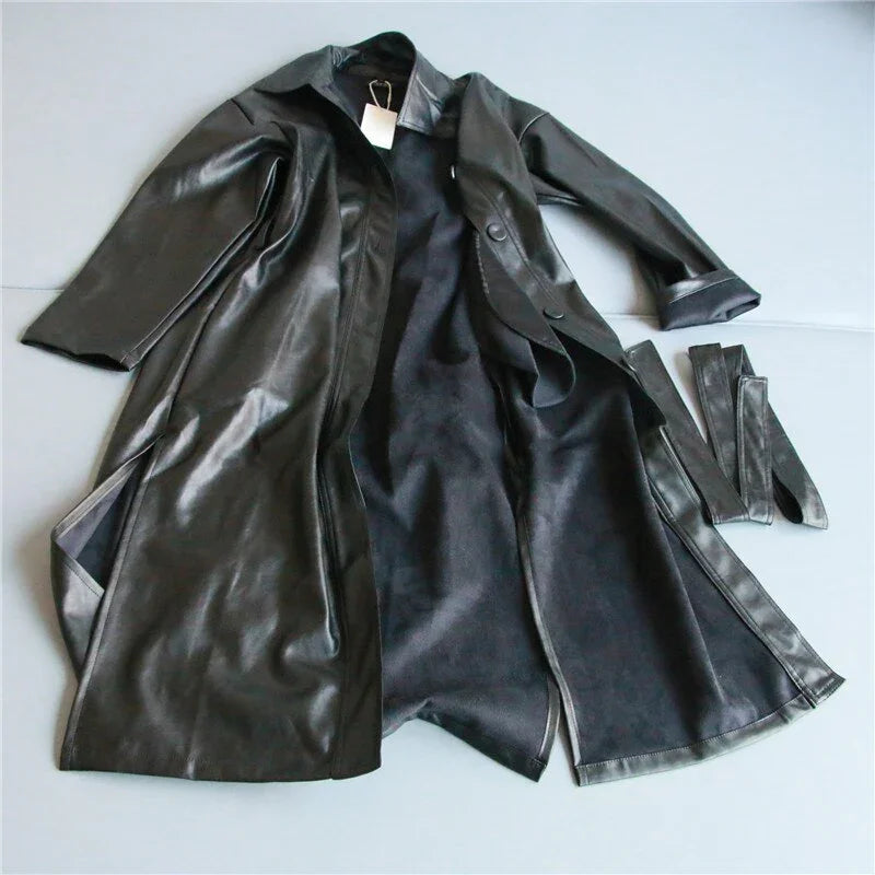 Black leather trench coat with matching belt laid open on a light surface
