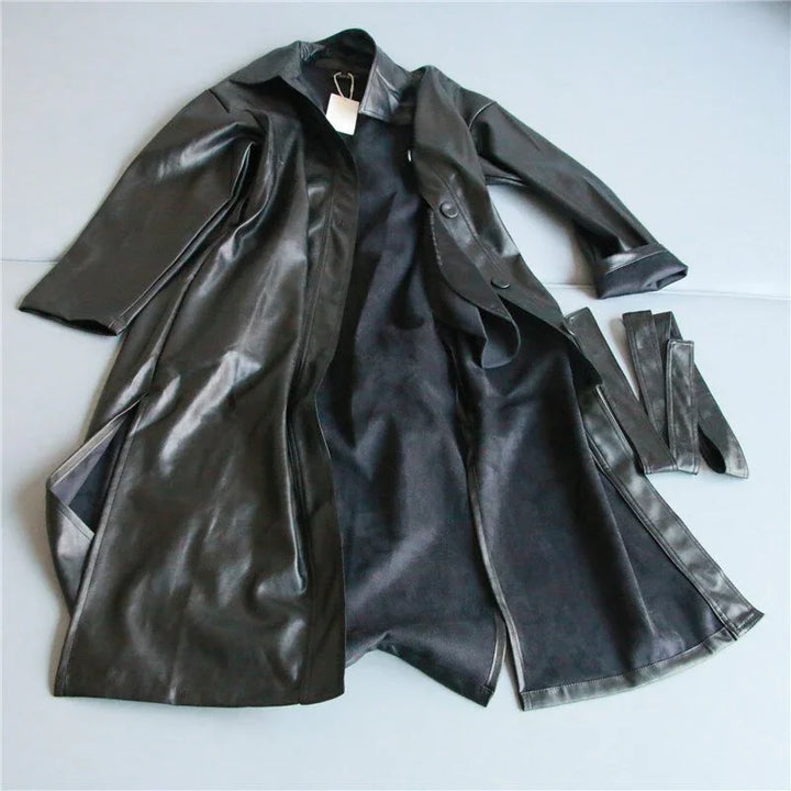Black leather trench coat with matching belt laid open on a light surface
