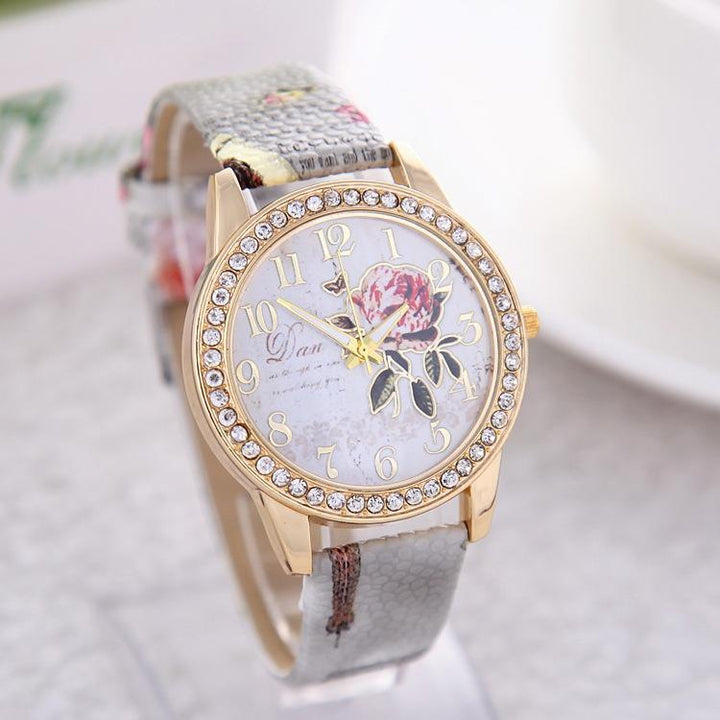 Women's gold-tone wristwatch with crystal bezel, floral dial design, and textured leather strap