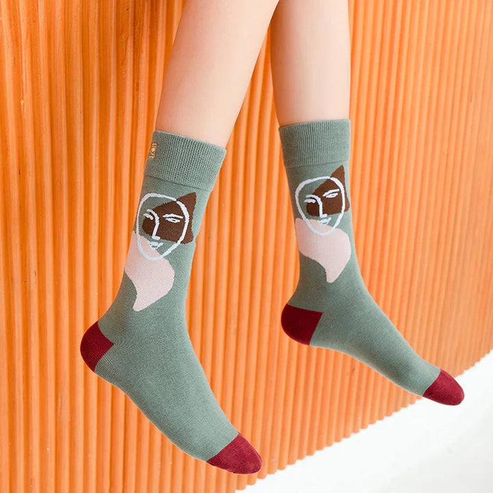 Green socks with abstract face design and maroon heel and toe against orange ribbed background