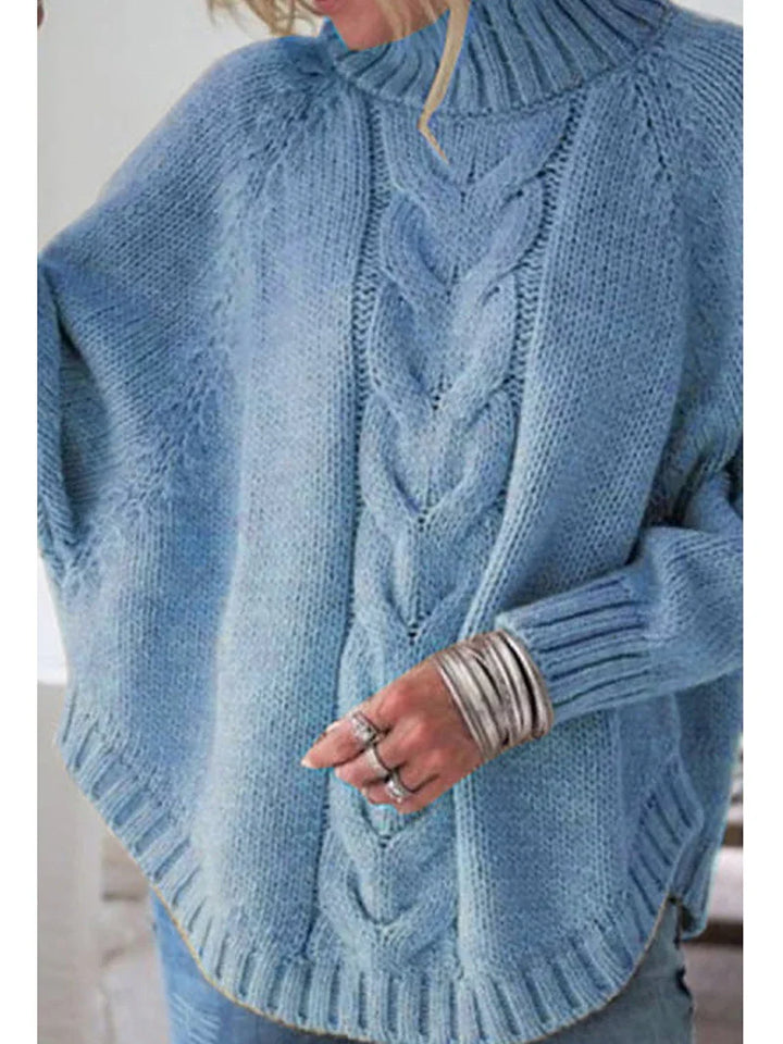 Close-up of a person wearing a cozy blue cable knit sweater with a ribbed high collar and silver stacked bangles